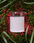 Lifestyle shot top view of Laboratory Perfumes Tonka Candle on grass with pink berries in the background