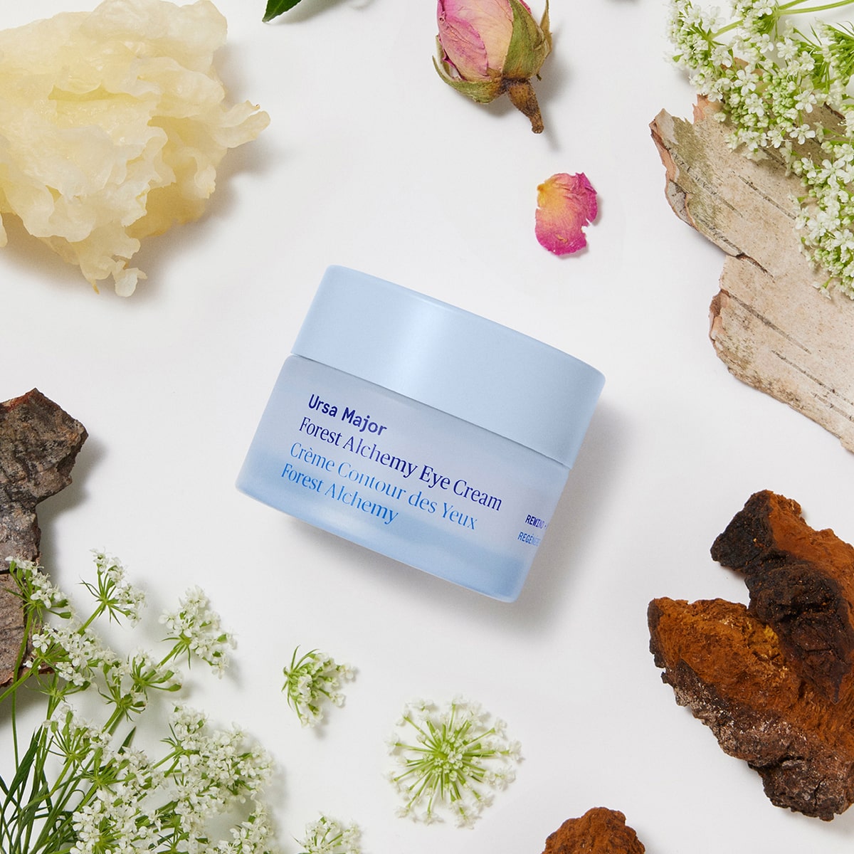 Ursa Major Forest Alchemy Eye Cream (0.5 oz) - product surrounded by flowers and wood. 