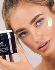Model holding jar of Odacite Green Smoothie Quenching Creme and showing smear on face