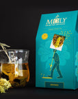 Lifestyle shot of MOLY The Mythic Antidote Defence Organic Herbal Tea with tea in glass cup next to box of Defence tea