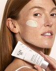 Model holding bottle of Top view of Yon-Ka Paris Sensitive Creme Anti-Redness (50 ml) and product smear on cheek to show green color and texture