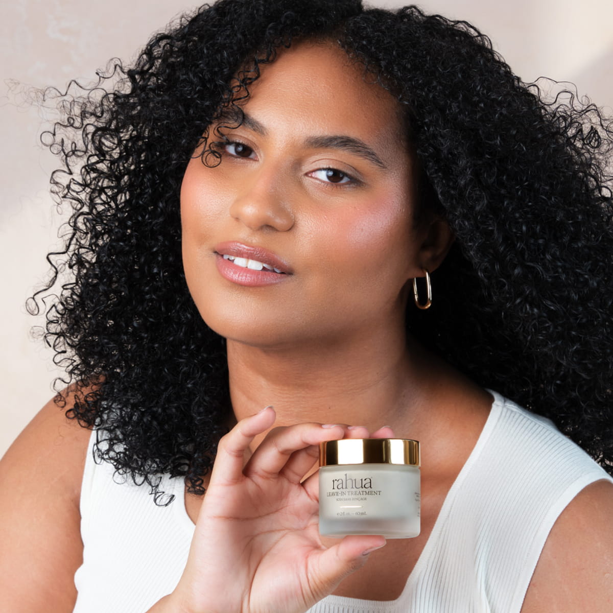 A woman with voluminous curly black hair holds a jar of Rahua Leave-In Treatment (60 ml)