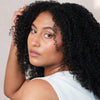 A close-up portrait of a woman with voluminous, tightly curled black hair, after using Rahua Leave-In Treatment