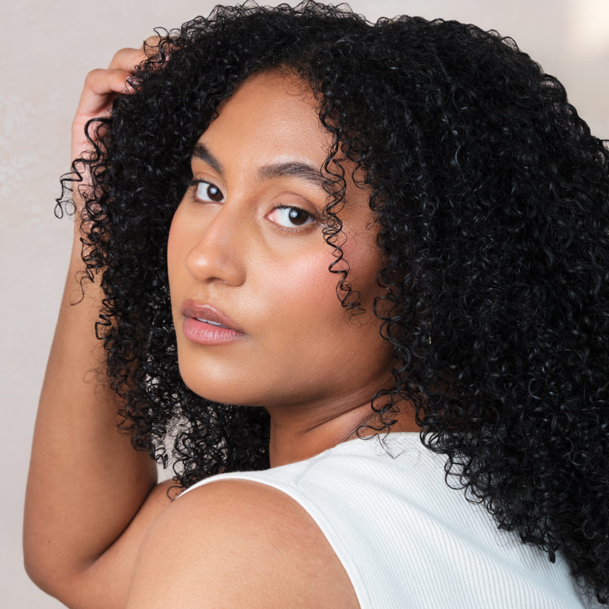 A close-up portrait of a woman with voluminous, tightly curled black hair, after using Rahua Leave-In Treatment