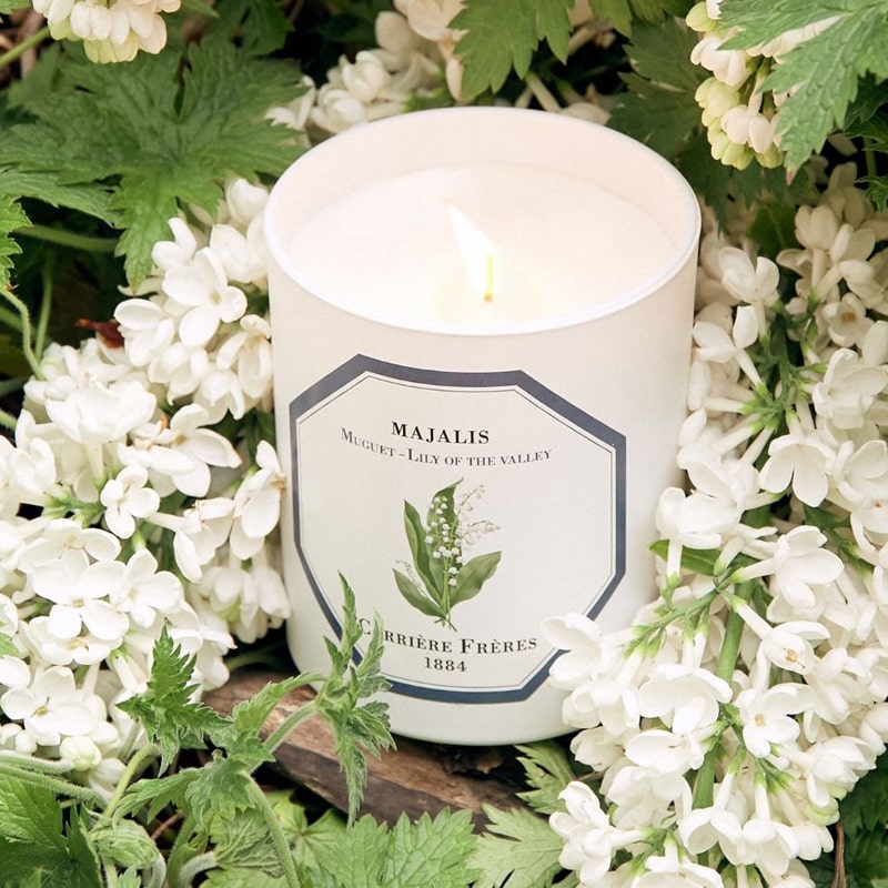 Lifestyle shot of Lily of the Valley Candle (185 g) shown lit with lily of the valley in the background