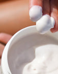 Close up shot of Carthusia A’mmare Body Lotion (250 ml) with lid off and model showing color and texture of lotion on fingertips
