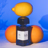Lifestyle shot of BDK Parfums Villa Neroli Eau de Parfum (100 ml) with lemon on top of bottle and oranges in the background