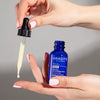 Close up of model holding dropper of Odacite Retinol + Hyaluronic Acid Renewing Serum and bottle with drop dispensing from dropper onto finger