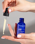 Close up of model holding dropper of Odacite Retinol + Hyaluronic Acid Renewing Serum and bottle with drop dispensing from dropper onto finger