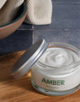 Lifestyle shot of Amber Cream jar open with lid off to the side showing cream color and texture