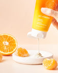 Model squeezing Yon-Ka Paris Lait Hydratant Vitality – Mandarin on dish with oranges in the background and foreground