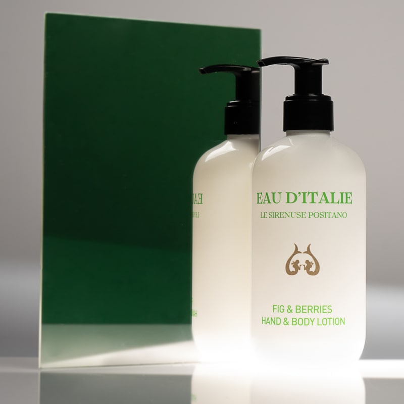 Lifestyle shot of Eau d’Italie Fig &amp; Berries Hand &amp; Body Lotion (300 ml) in front of mirror with dark green background reflection