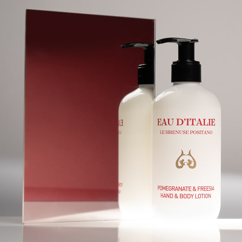 Lifestyle shot of Eau d’Italie Pomegranate &amp; Freesia Hand &amp; Body Lotion (300 ml) in front of mirror with red background reflection