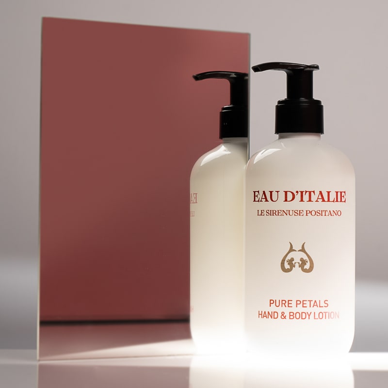 Lifestyle shot of Eau d’Italie Pure Petals Hand &amp; Body Lotion (300 ml) in front of mirror with pink background reflection