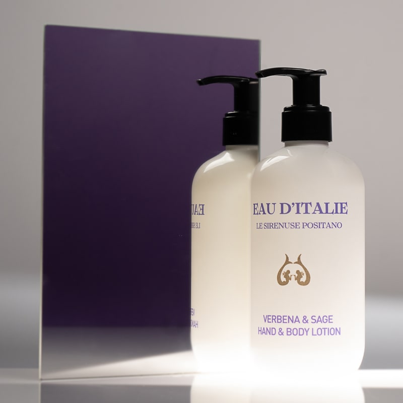 Lifestyle shot of Eau d’Italie Verbena &amp; Sage Hand &amp; Body Lotion (300 ml) in front of mirror with dark purple background reflection
