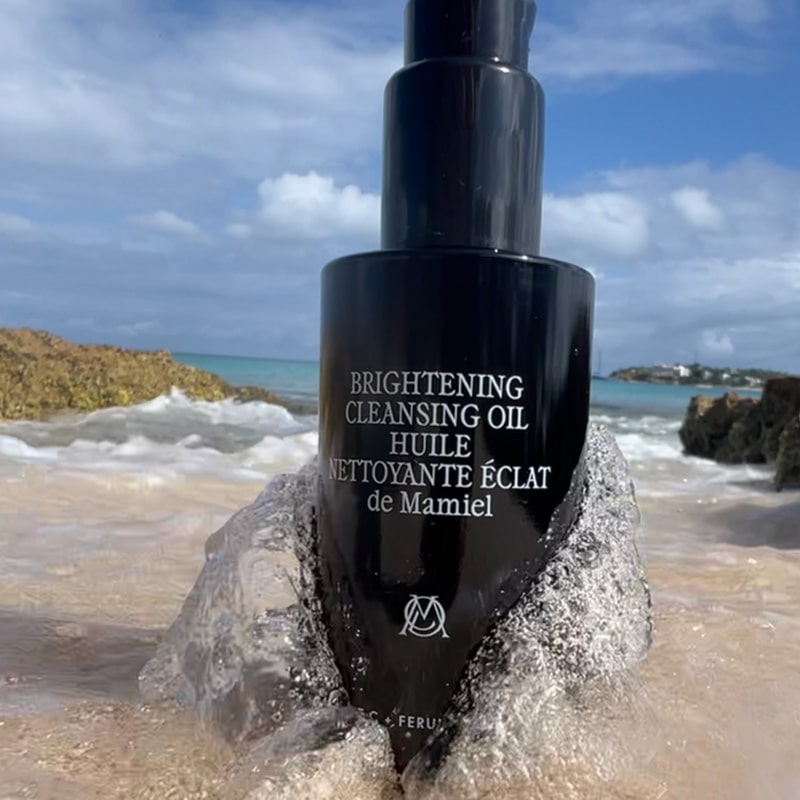 Lifestyle shot of de Mamiel Brightening Cleansing Oil (100 ml) on sandy beach with ocean in the background