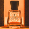 Lifestyle shot of Frapin Attendre & Esperer Eau de Parfum with bricks on either side of the bottle and bright orange background