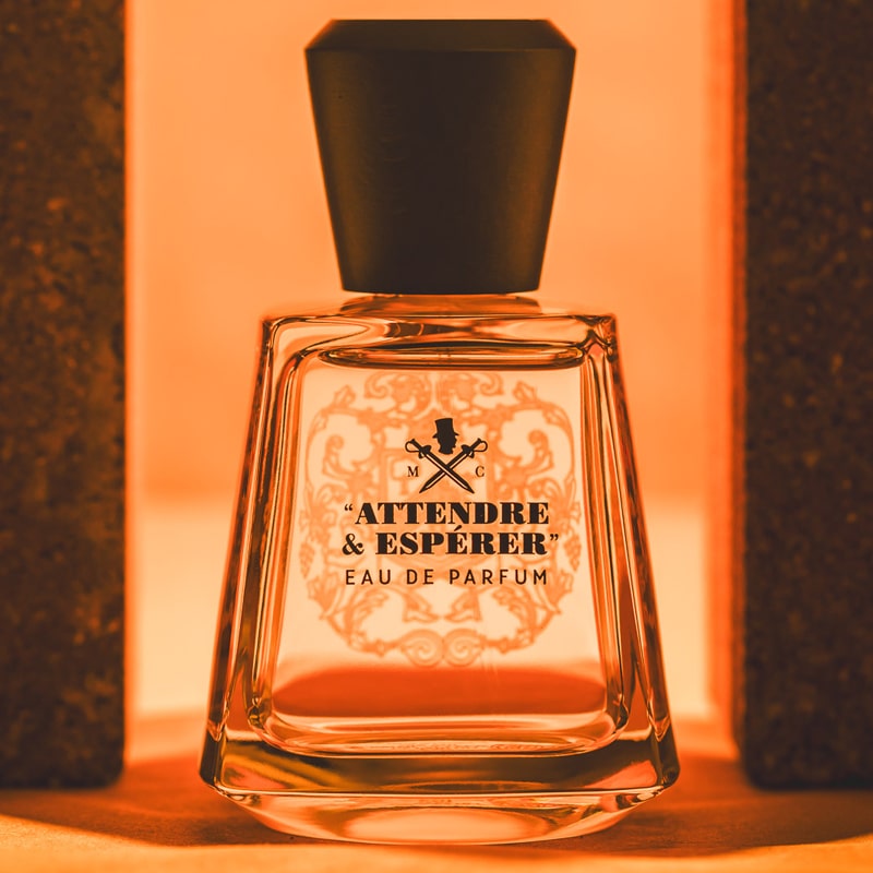 Lifestyle shot of Frapin Attendre & Esperer Eau de Parfum with bricks on either side of the bottle and bright orange background