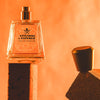 Lifestyle shot of Frapin Attendre & Esperer Eau de Parfum with cap off sitting on the end of a brick and bright orange background