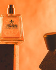 Lifestyle shot of Frapin Attendre & Esperer Eau de Parfum with cap off sitting on the end of a brick and bright orange background