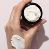 Close up of model holding opened jar of Odacite Jojoba Pearls Daily Hydra-Exfoliant (50 ml) and product smear on hand