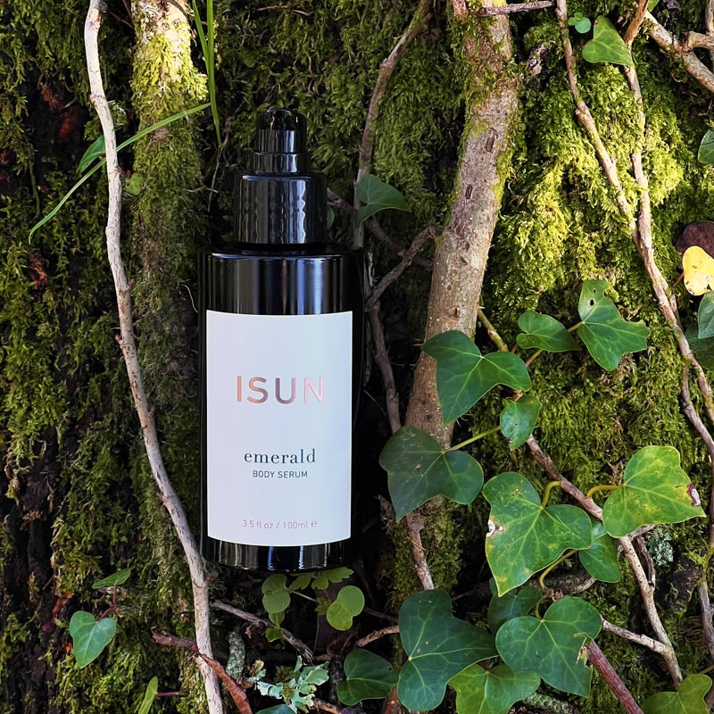 Lifestyle shot of ISUN Emerald Body Serum (100 ml) with mossy tree and ivy in the background