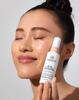 Model holding bottle of Odacite SPF 50 Flex-Perfecting™ Mineral Drops Tinted Sunscreen (30 ml) - TWO