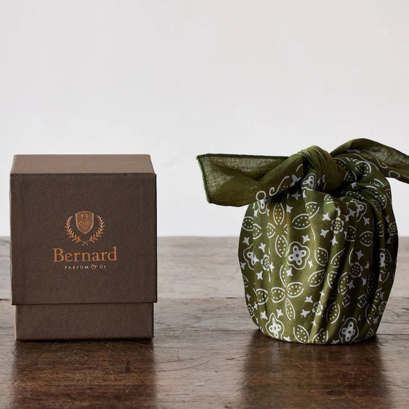 Bernard Parfum Meli Candle - Product displayed on wood table with cloth and packaging 