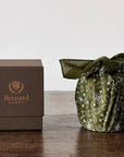 Bernard Parfum Meli Candle - Product displayed on wood table with cloth and packaging 