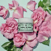 Lifestyle shot of Santa Maria Novella Acqua di Rose Cream (50 ml) shown with pink roses and leaves in the background