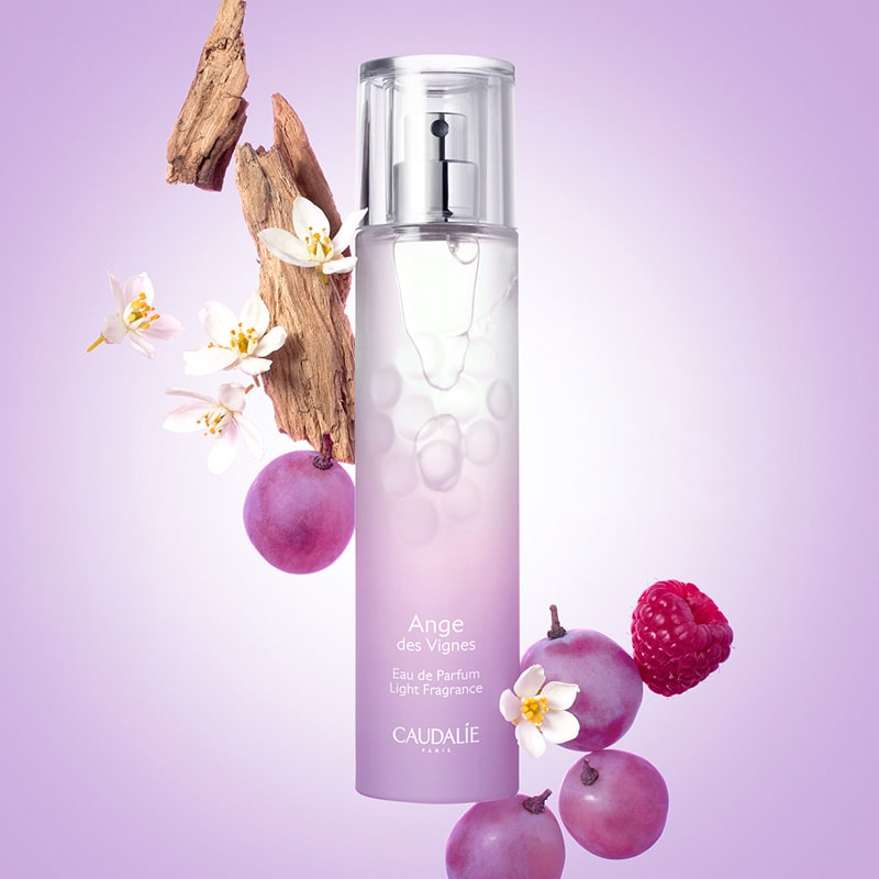 Lifestyle shot of Caudalie Ange des Vignes Light Fragrance (50 ml) with grapes, raspberry, flowers and bark in the background