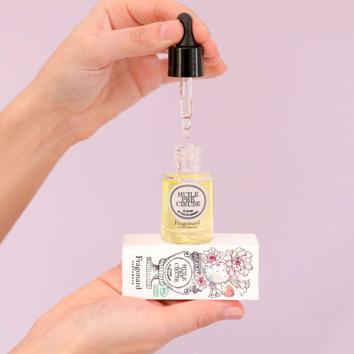 Fragonard Parfumeur Precious Oil - Prickly Pear Seed (15 ml) with box - product shown being held on pink background. 