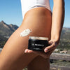 Le Prunier Plumbody - Lifestyle photo of model holding body cream container, with swatch on leg