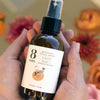 8 Days Botanicals Love Botanical Room Spray - model holding bottle with flowers in background