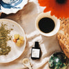 Versatile Paris Culot The (Tea Cap) Extrait de Parfum beside a cup of tea and a plate with grapes 