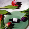 Versatile Paris Culot The (Tea Cap) Extrait de Parfum on a plate surrounded by tulips