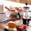 Versatile Paris Dimanche Flemme (Lazy Sunday) Extrait de Parfum on kitchen table with coffee, bread sticks and other food