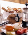 Versatile Paris Dimanche Flemme (Lazy Sunday) Extrait de Parfum on kitchen table with coffee, bread sticks and other food