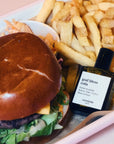 Versatile Paris God Bless Cola Extrait de Parfum shown in a tray with French Fries and a Hamburger