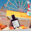 Versatile Paris God Bless Cola Extrait de Parfum shown in a box with Hot Dogs with a Ferris Wheel in the background
