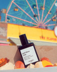 Versatile Paris God Bless Cola Extrait de Parfum shown in a box with Hot Dogs with a Ferris Wheel in the background