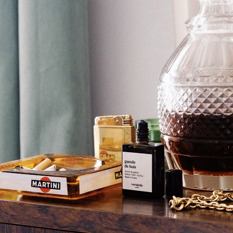 Versatile Paris Gueule de Bois (Hangover) Extrait de Parfum between an ashtray and a bottle of liquor