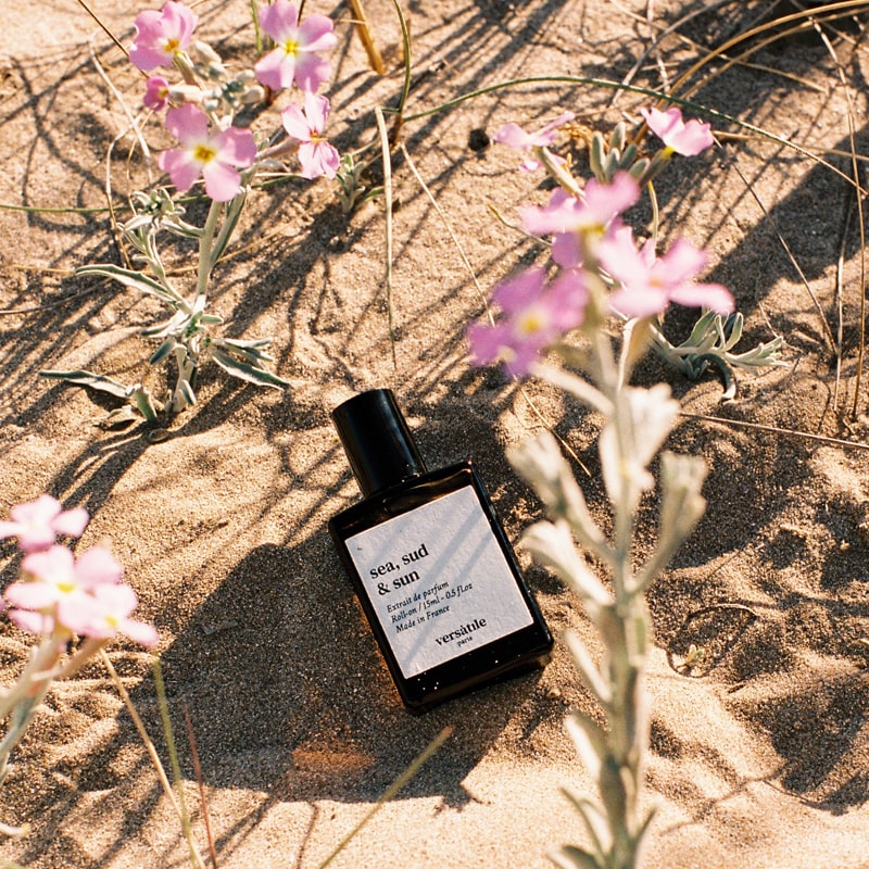 Versatile Paris Sea, Sud &amp; Sun (Sea, South &amp; Sun) Extrait de Parfum shown on sand by wildflowers