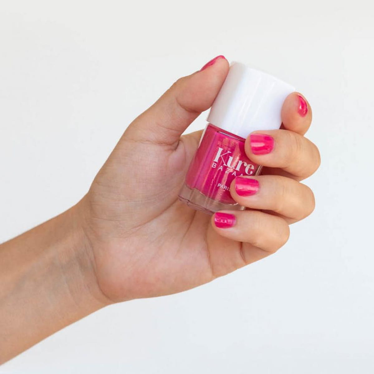 Close up of model wearing Kure Bazaar Nail Lacquer - Kelly (10 ml) and holding bottle