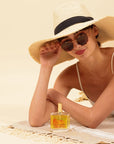 LES PANACEES Nourishing Dry Body and Hair Oil - Summer Essence - hair oil shown next to model laying on towel on sand