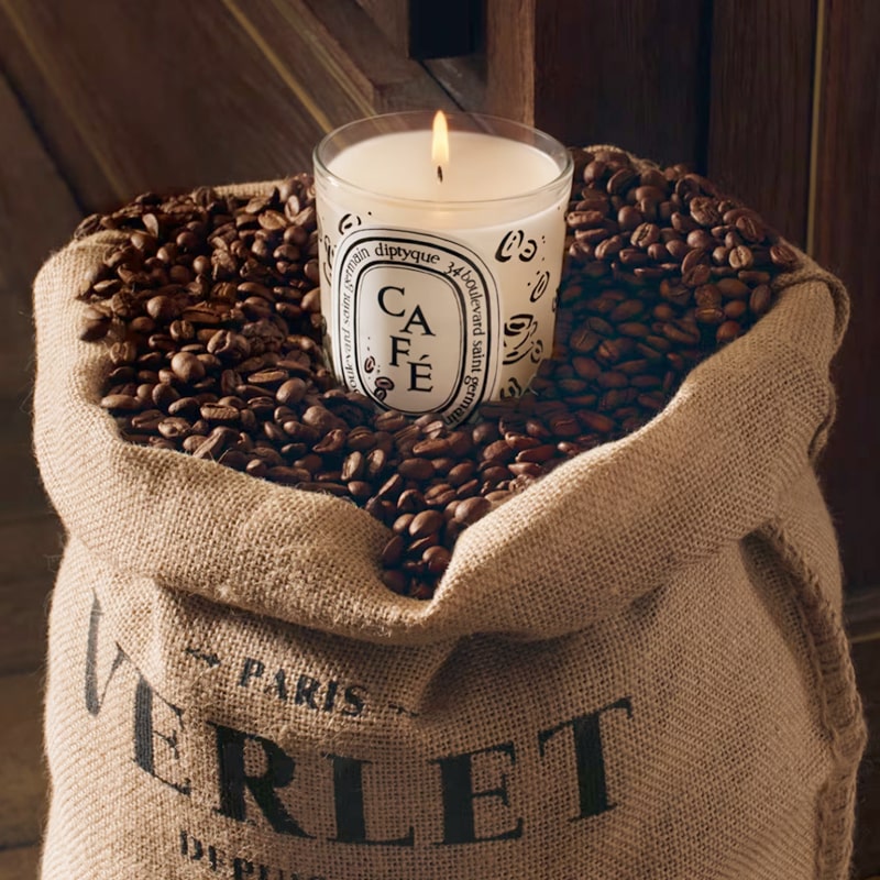 Lifestyle shot of Diptyque Cafe (Coffee) Candle (190 g) sitting in a Verlet Paris Cafe sack opened and filled with whole coffee beans