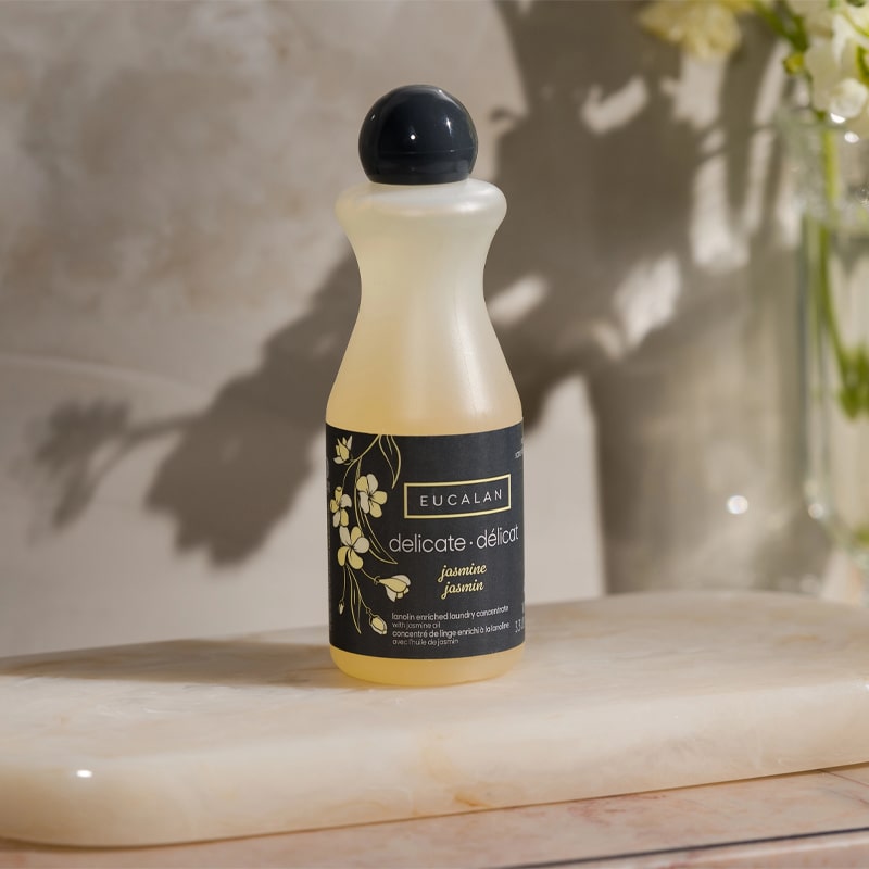 Eucalan Jasmine Delicate Wash - Lifestyle shot of Delicate Wash bottle on stone display by glass vase and flowers