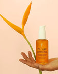 Rahua Enchanted Island Body Glow Serum - Product shown in models hand with flower in background