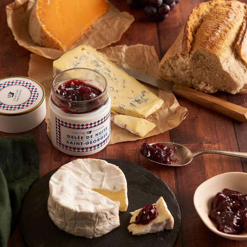 Confiture Parisienne Nuits Saint Georges Jelly - Jelly jar shown open surrounded by cheeses and bread on wood table