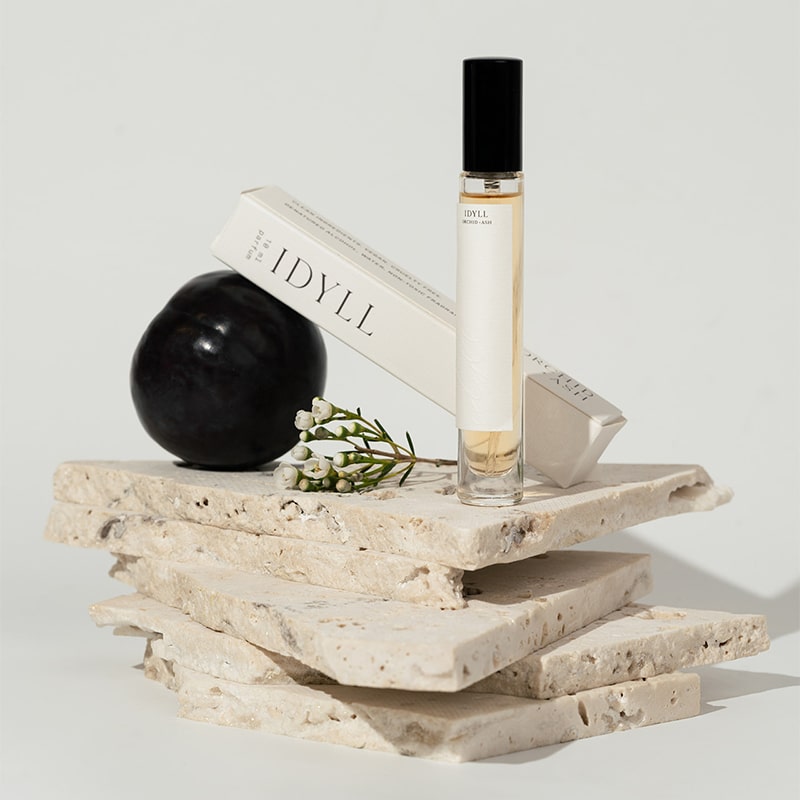 Orchid + Ash Idyll Perfume Travel Spray - Jasmine Incense + Vanilla - product and packaging shown on top of stone slabs with fragrance ingredients 